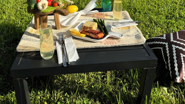 Een picknickopstelling in een grasveld met een tafel, eten en drinken.