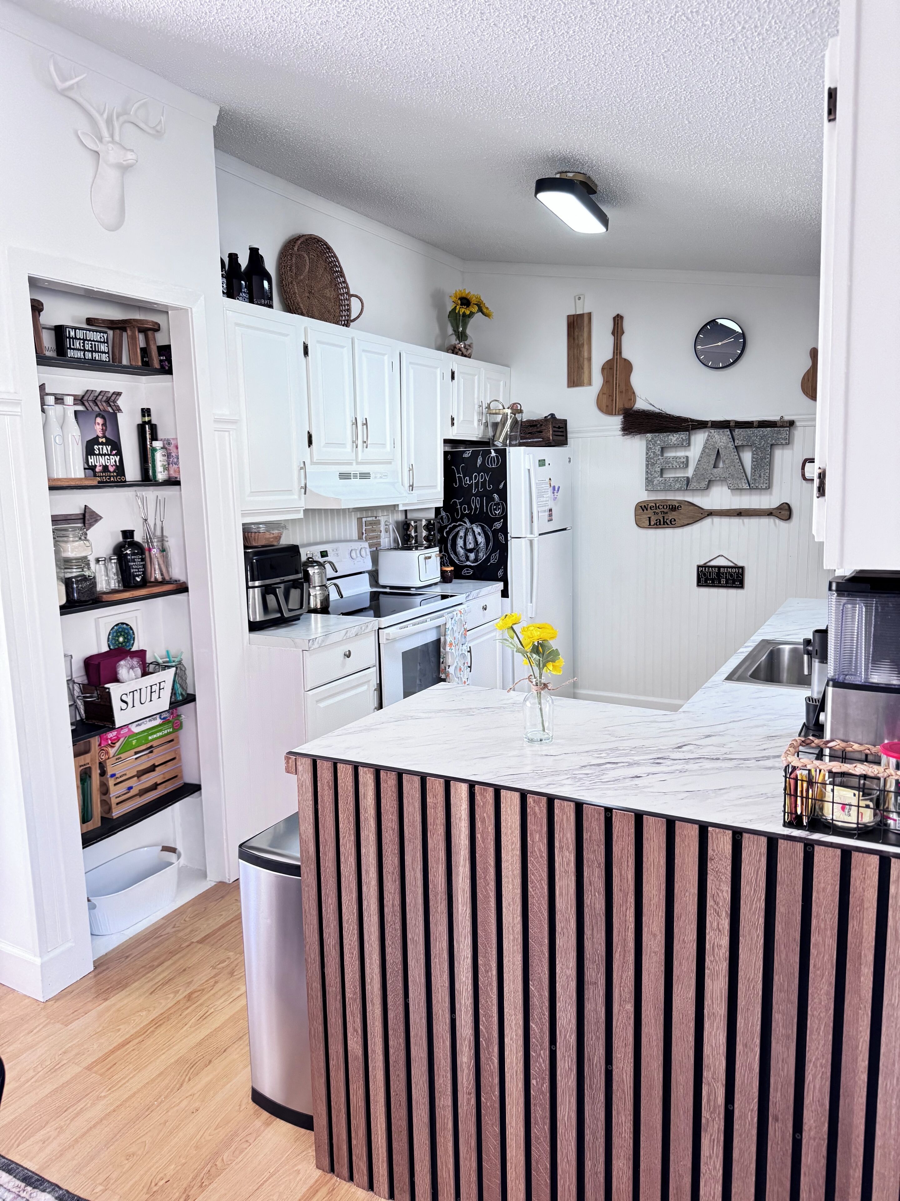 Une cuisine moderne avec des meubles blancs, un îlot central et un mur d’accent en bois rustique.