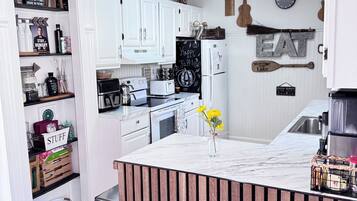 Une cuisine moderne avec des meubles blancs, un îlot central et un mur d’accent en bois rustique.