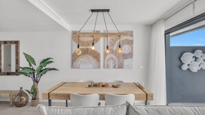 Un espace repas moderne avec une table en bois, des chaises à revêtement gris et un luminaire suspendu.