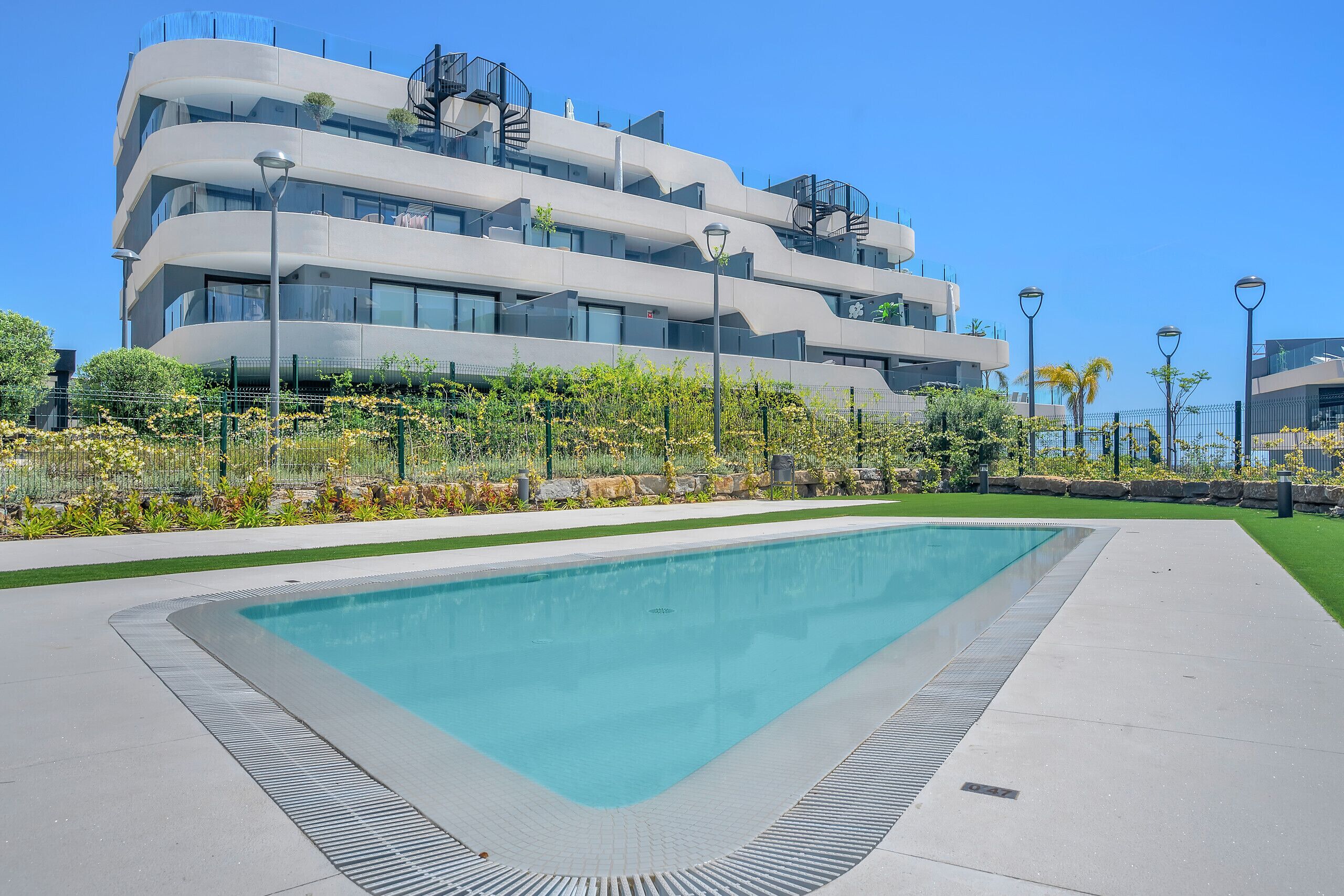Un edificio moderno con piscina, rodeado de un jardín cuidado y farolas.