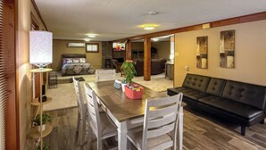A spacious living room with a wooden dining table, white chairs, a black leather sofa, and a television. - Waterfront Retreat on Raymond Gary State Lake (Fort Towson)