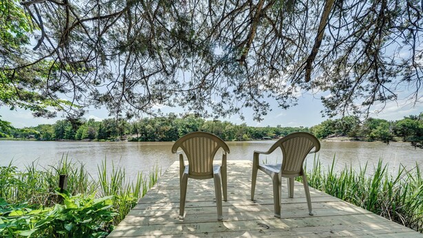 A wooden dock with two wicker chairs facing a calm river, surrounded by greenery and trees. - Waterfront Retreat on Raymond Gary State Lake (Fort Towson)