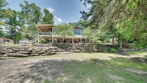 A two-story house with a stone retaining wall, a covered porch, and a large lawn. - Waterfront Retreat on Raymond Gary State Lake (Fort Towson)