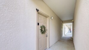 A hallway with a door adorned with a wreath, leading to a corridor with a light fixture on the wall. - 'Mountain Escape' w/ Pool Access in Pigeon Forge! (Pigeon Forge)