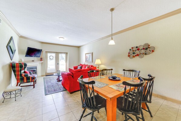 A dining area with a wooden table and black chairs, a red sofa, a television mounted on the wall, and a fireplace. - 'Mountain Escape' w/ Pool Access in Pigeon Forge! (Pigeon Forge)