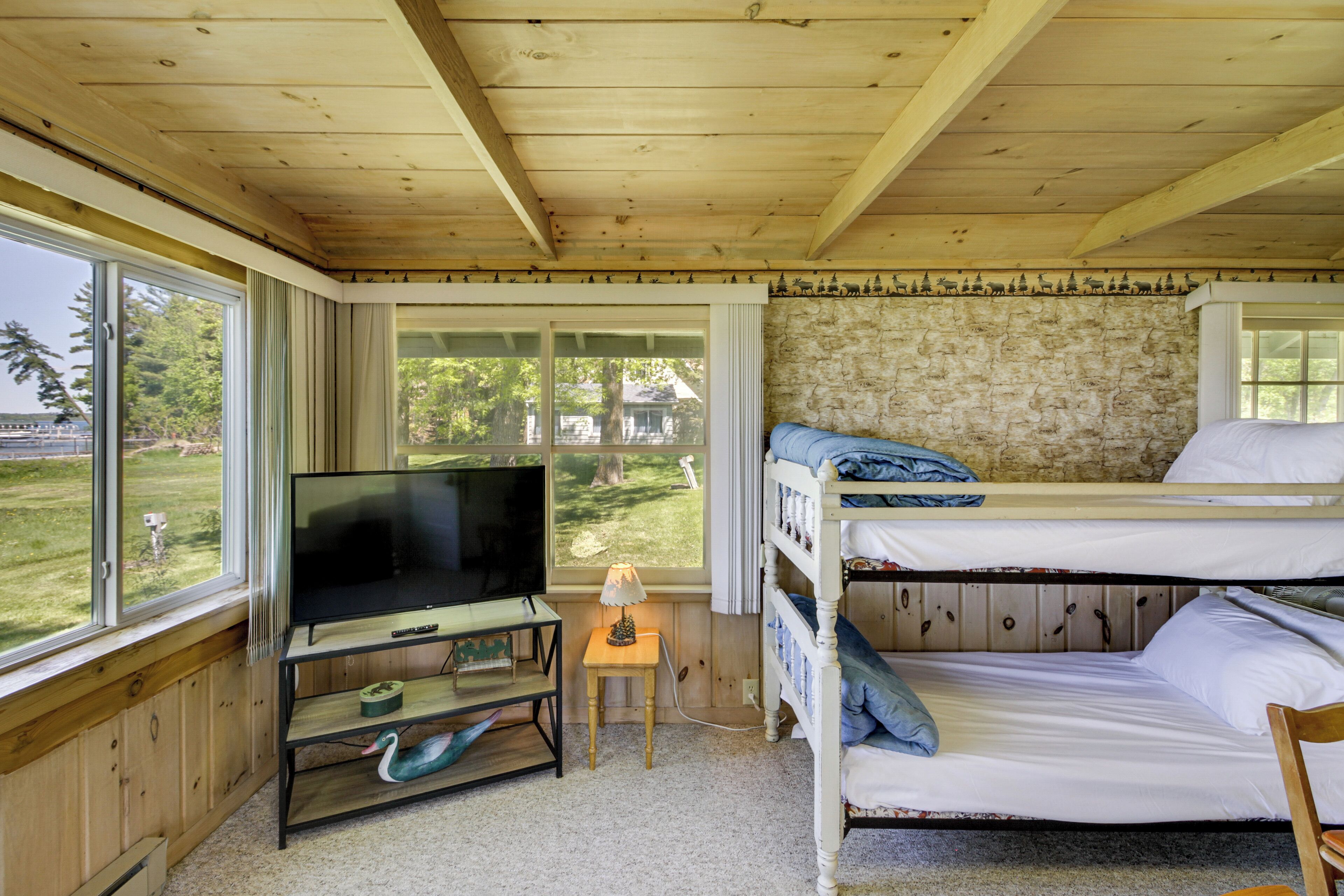 A room with a television, bunk beds, a small table with a lamp, and a view of the outdoors.