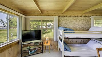 A room with a television, bunk beds, a small table with a lamp, and a view of the outdoors.