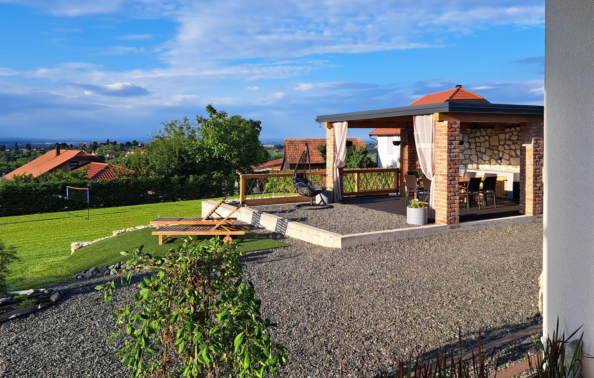 A patio area with a hanging chair, a table with chairs, and a view of the surrounding landscape.