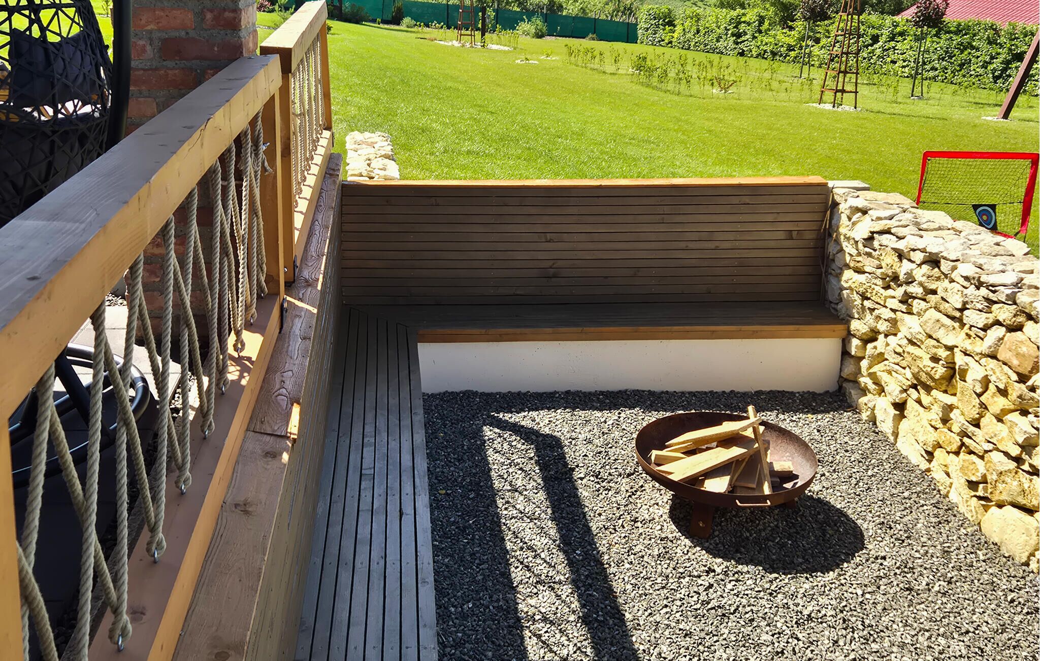 A wooden deck with a bench, a fire pit, and a stone wall.