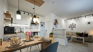 Een moderne keuken met witte kasten, een eettafel gedekt voor vier personen en een zithoek met een bank en een viool.