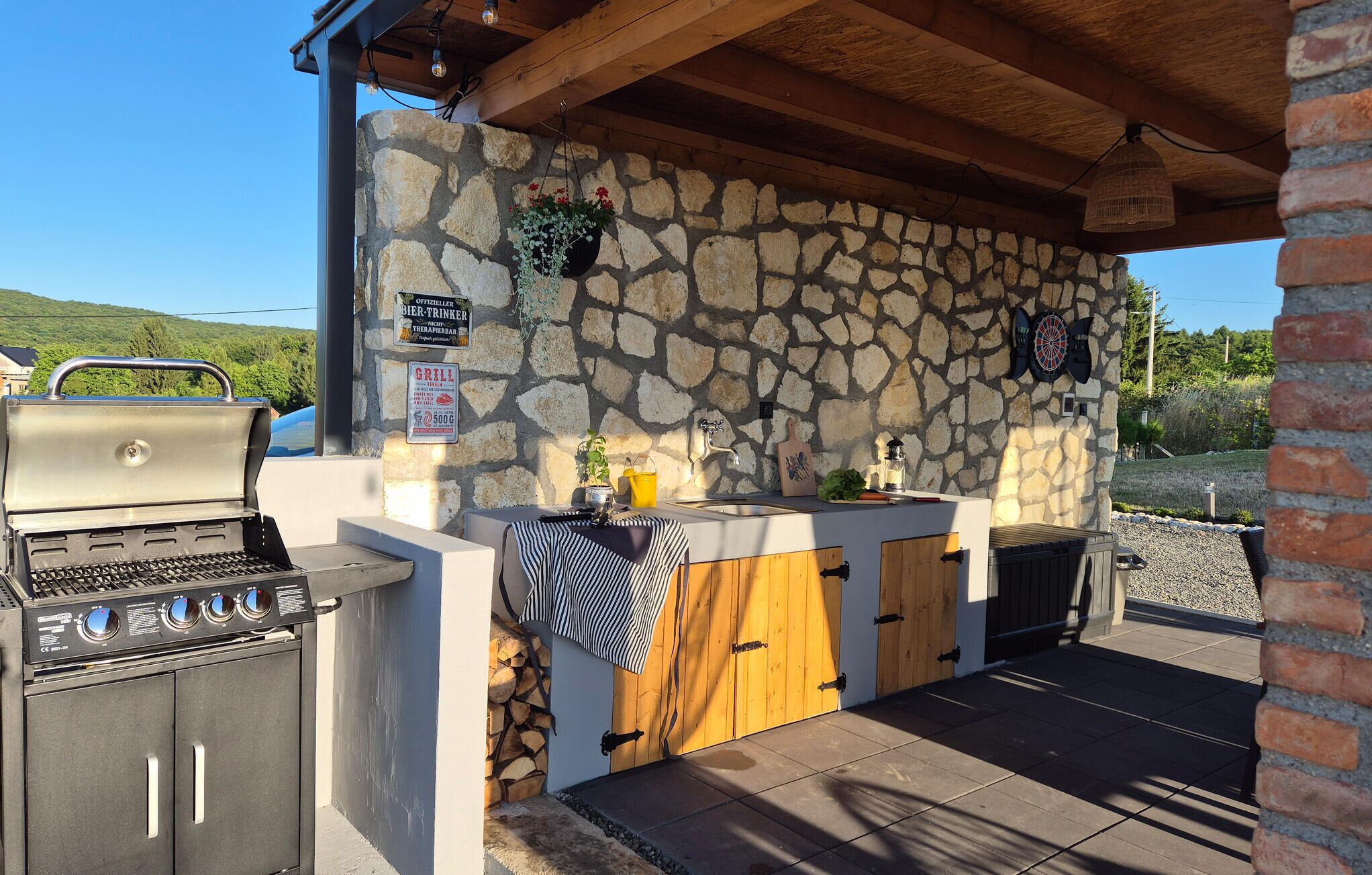An outdoor kitchen area with a stone wall, a grill, a sink, and a wooden door.