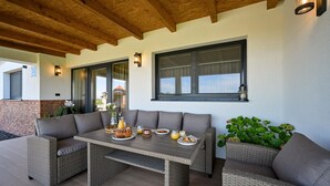 Een terras met rieten meubilair, een gedekte tafel met borden, glazen en een lantaarn.