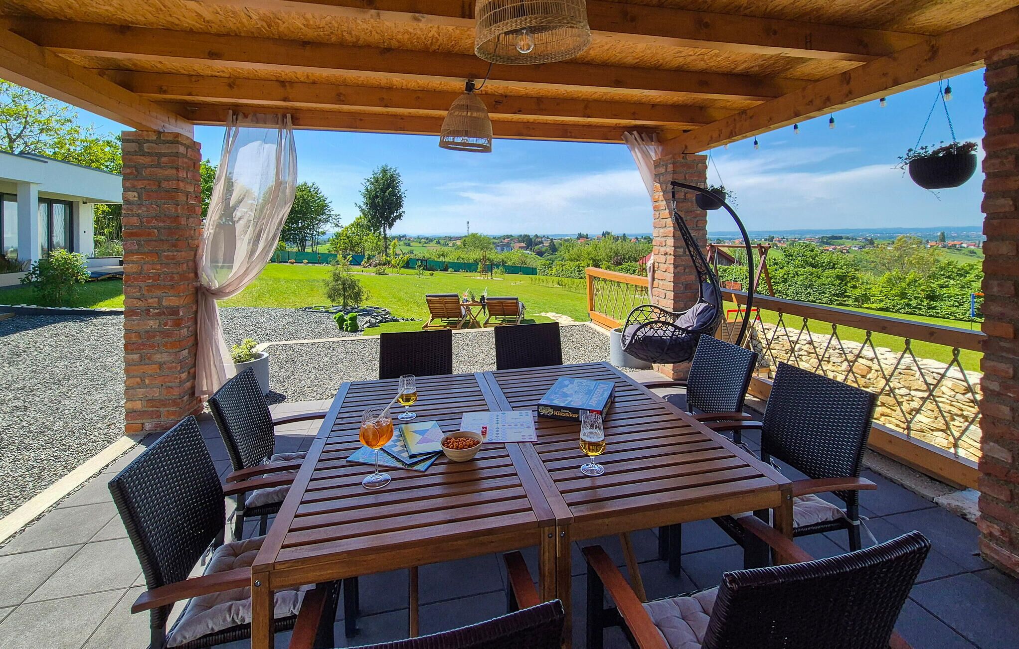 Une table en bois avec des chaises, un fauteuil suspendu et une vue sur un paysage verdoyant.