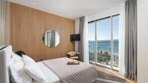 A modern hotel room with a large bed, a wooden panel wall, a round mirror, a TV, and a balcony with a view of the sea. - Beautiful home in Turanj (Turanj)