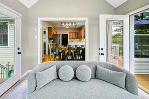 A modern living room with a grey sofa, a dining area with wooden chairs, and a view of the backyard through a sliding glass door. - Lakefront Lake Anna, Dock, Views, Deck, Movies (Mineral)