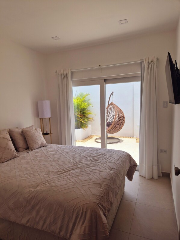 Une chambre avec un grand lit, un fauteuil suspendu et une vue sur l’extérieur.