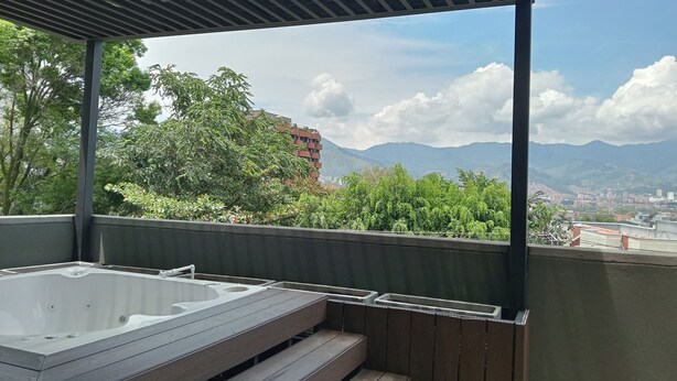 Un balcón con jacuzzi, escalones de madera y vistas a montañas y una ciudad.