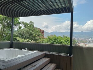 A balcony with a hot tub, wooden steps, and a view of mountains and a cityscape. - Hotel Rulay Medellin (Medellín)