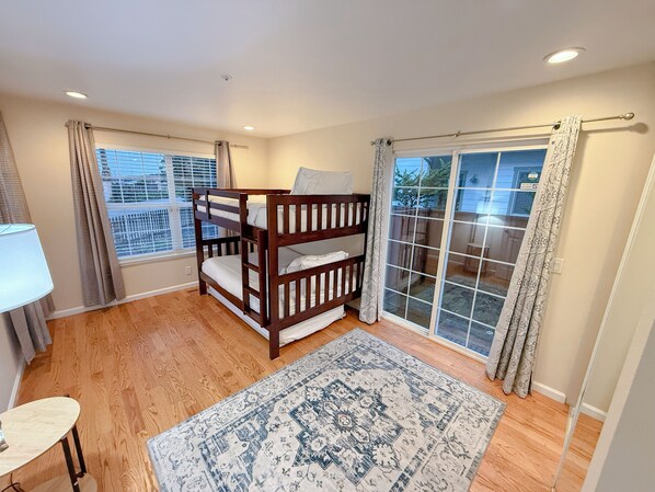 A room with a bunk bed, a window with blinds, a door with a glass panel, and a patterned rug. - Gorgeous Half Moon Bay Home (El Granada)