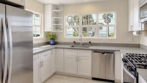 A modern kitchen with white cabinets, a stainless steel refrigerator, a dishwasher, and a gas stove. - Gorgeous Half Moon Bay Home (El Granada)