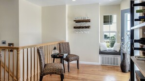 A living room with a wooden staircase, two wicker chairs, a small table with a lamp, a wall-mounted wine rack, and a large window with a view of the outside. - Gorgeous Half Moon Bay Home (El Granada)