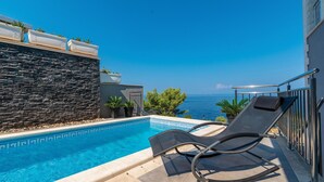 A poolside area with a view of the sea, a stone wall, and a lounge chair.