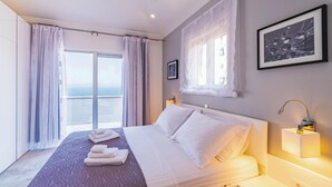 A hotel room with a bed, a window with sheer curtains, a framed picture on the wall, and a view of the sea.