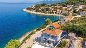 A coastal village with houses along the shoreline, clear blue sea, and hilly background.