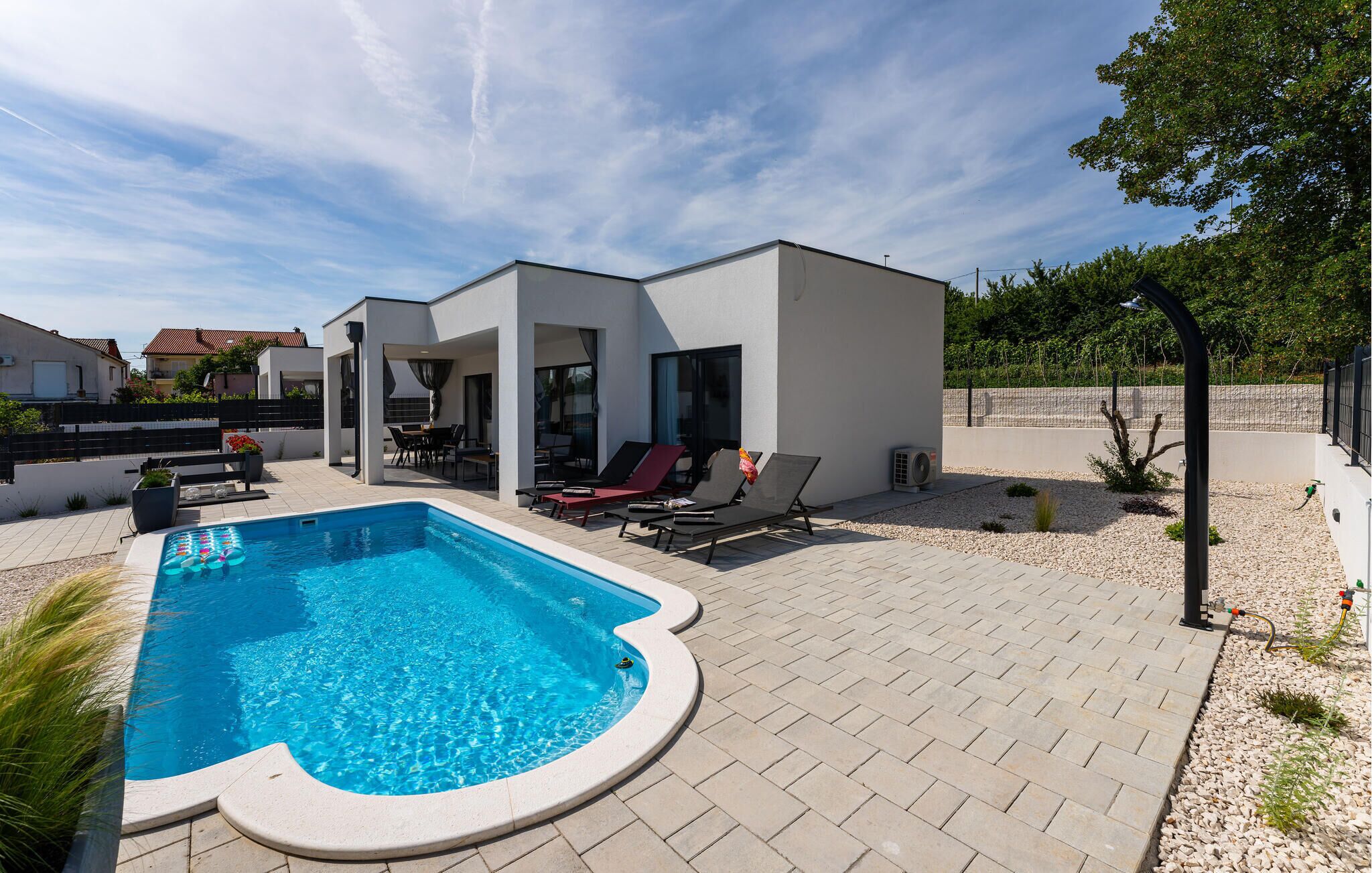 Ett modernt hus med en swimmingpool, utomhusmöbler och en trädgård.