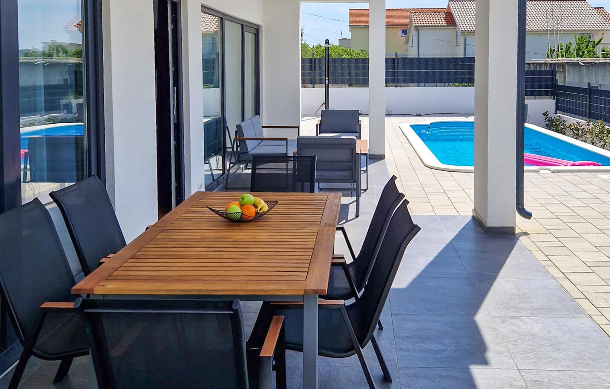 Une terrasse avec une table et des chaises en bois, une piscine et une vue sur les environs.
