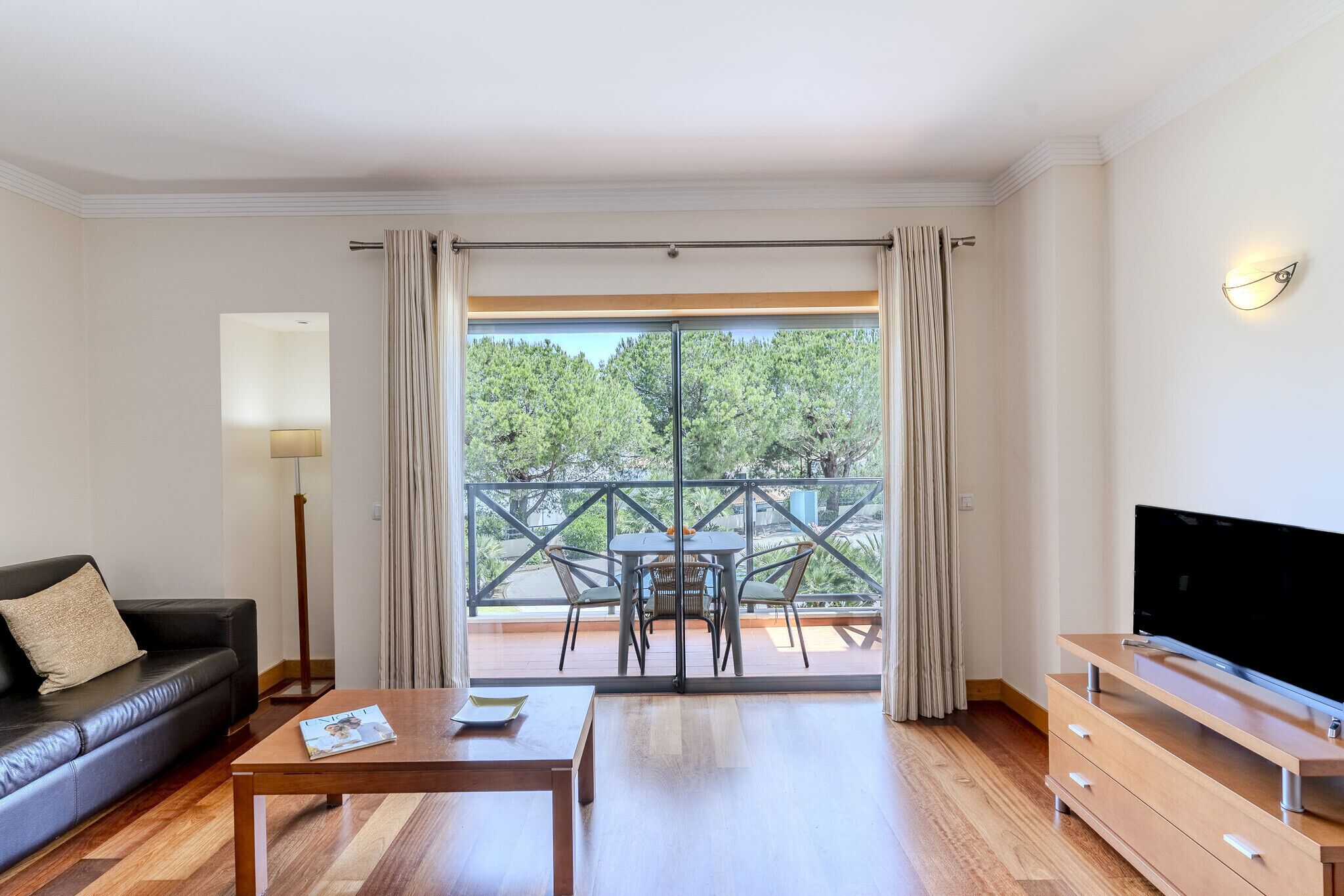A modern living room with a sofa, coffee table, TV stand, and a balcony with a table and chairs.