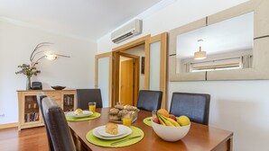 A dining area with a wooden table, chairs, a fruit bowl, a croissant, and a glass of orange juice.