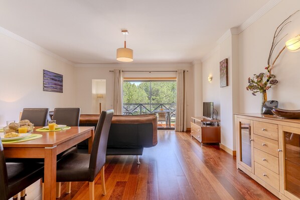 A modern dining area with a wooden table, black chairs, and a view of the outdoors through large windows.