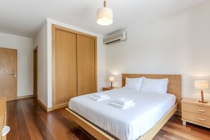 A neatly arranged hotel room with a large bed, wooden wardrobe, bedside tables, and a ceiling light.
