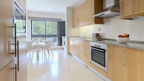 A modern kitchen with wooden cabinets, a stainless steel oven, and a dining area with a table and chairs.