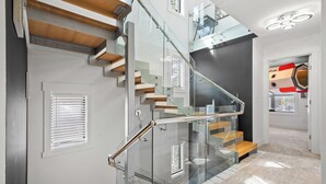 A modern staircase with glass railings and wooden steps, leading to an upper floor. - *Spectacularly Spacious*  6-Person Sauna |Rocket-ship|Game-Room|Hammock (Calgary)
