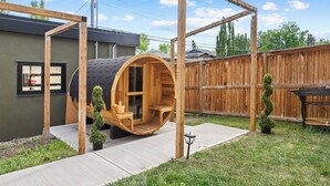 A wooden hot tub structure in a backyard with a wooden fence and a small tree. - *Spectacularly Spacious*  6-Person Sauna |Rocket-ship|Game-Room|Hammock (Calgary)