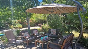 Een terras buiten met een houten tafel, vier stoelen en een grote parasol.