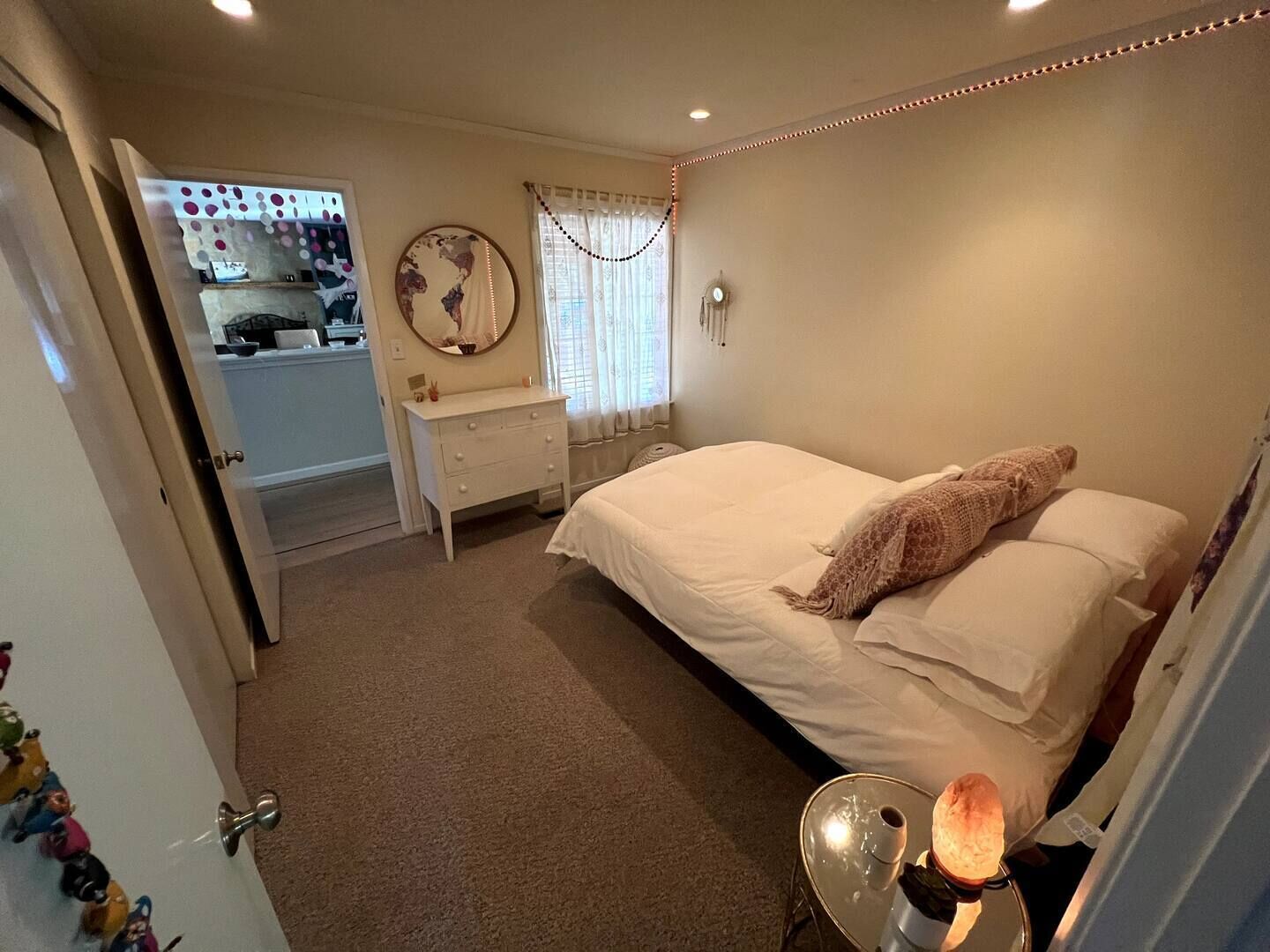 Un dormitorio con cama, cómoda, espejo y ventana con cortinas.