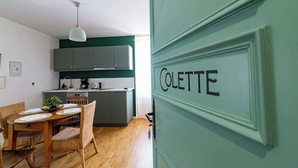 A modern kitchen with grey cabinets, a dining table with chairs, and a hanging light fixture. - Logis Colette (flavigny sur Ozerain)