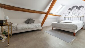 A loft bedroom with a slanted ceiling, a bed, a sofa, a desk, and a wall mural. - Logis Colette (flavigny sur Ozerain)