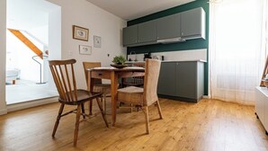 A dining area with a wooden table and chairs, a kitchen with grey cabinets, and a view of a balcony. - Logis Colette (flavigny sur Ozerain)
