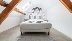 A bedroom with a sloped ceiling, a bed, a small bedside table, a nightstand, and a wall mural. - Logis Colette (flavigny sur Ozerain)