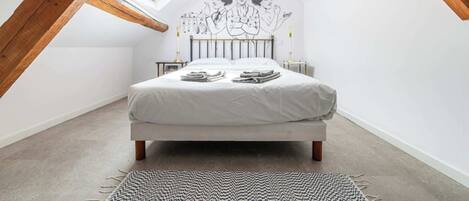 Un dormitorio con techo inclinado, una cama, una mesita de noche pequeña y un mural en la pared.