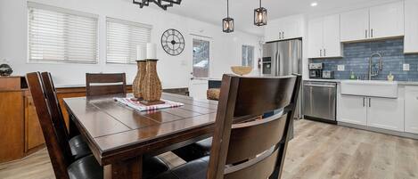 A modern kitchen with white cabinets, a stainless steel refrigerator, and a dining area with a wooden table and chairs.