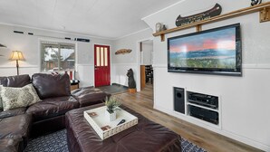 A modern living room with a leather sofa, a flat-screen TV mounted on the wall, and a fireplace. - Boulder Bay Bungalow (Big Bear Lake)