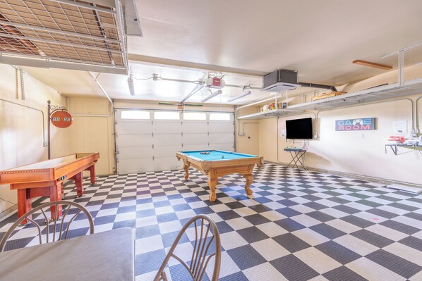 Una habitación con mesa de billar, sillas, un reloj y un cartel que indica una sala de juegos.