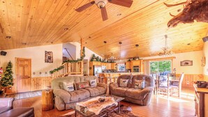 A spacious living room with leather sofas, a glass coffee table, and a wooden ceiling fan.