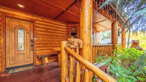 A wooden cabin with a wooden staircase, a door with a glass panel, and a porch area with greenery.